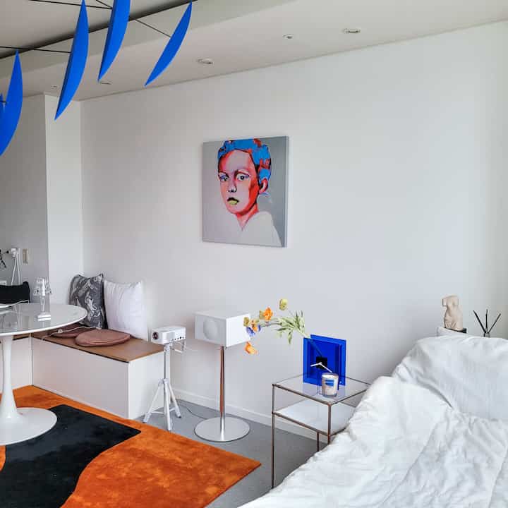 White and orange toned studio living room featuring minimal furniture and framed artwork in a simple modern space