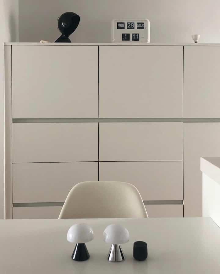 ホワイトトーンのキッチン、カスタムビルトインキャビネットとシンプルなテーブルに二つのキノコ型テーブルランプが配置された印象的で清潔感のある空間