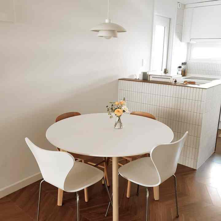 A warm kitchen space in white and brown tones featuring a round dining table with chairs and a vase of flowers at the center