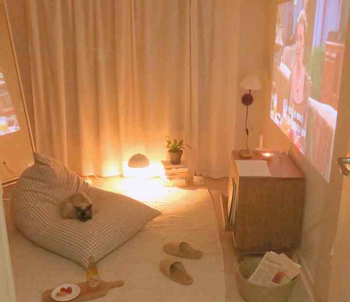 Warm beige-toned living room featuring a checkered bean bag sofa with a cat, wooden side table, and a projector screen on the wall creating a cozy home cinema atmosphere
