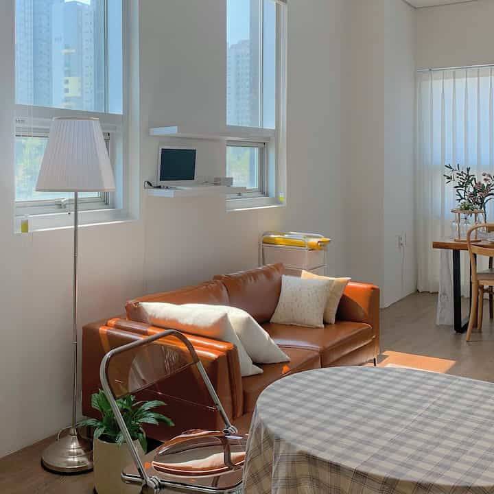 Bright white-toned studio apartment featuring brown leather sofa and wooden dining table in a natural atmosphere