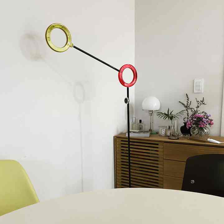 白い壁と木目調のキャビネット、赤と黄色のリングが特徴的なフロアランプのあるモダンなダイニングルーム