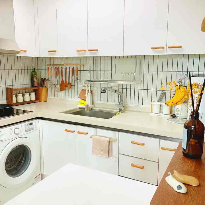 A small kitchen with white and natural wood tones, featuring tiled backsplash and neatly arranged kitchen utensils in a clean DIY interior style