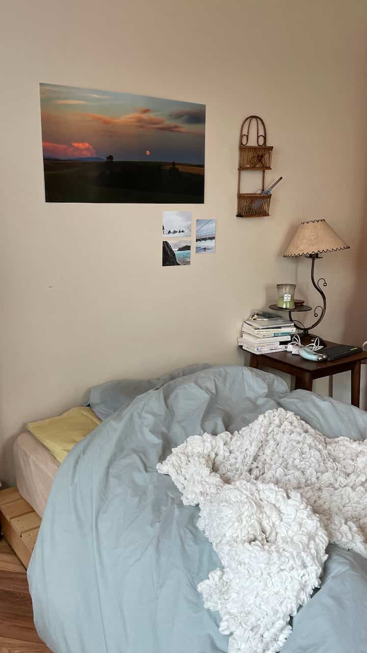 Calm beige-walled bedroom featuring a light blue duvet cover on bed and a wooden side table with books and lamp in a natural modern setting