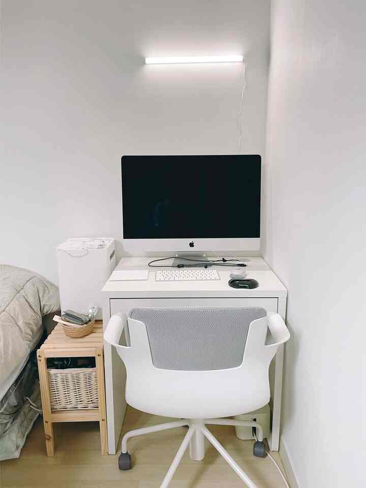 ホワイトと木目調が調和したコンパクトなワークスペース、机とオフィスチェア、LEDバー照明が配置された小さな作業部屋