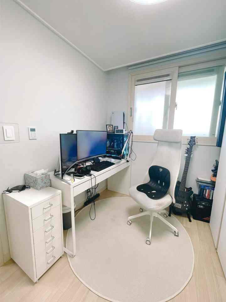 A compact home office in white and beige tones featuring a computer desk, office chair, and drawer storage in a neat small room