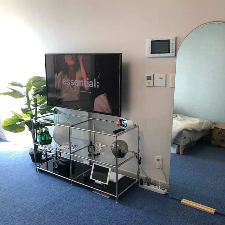 Modern studio apartment living area with blue carpet, white walls, featuring a wall-mounted TV and modular TV stand