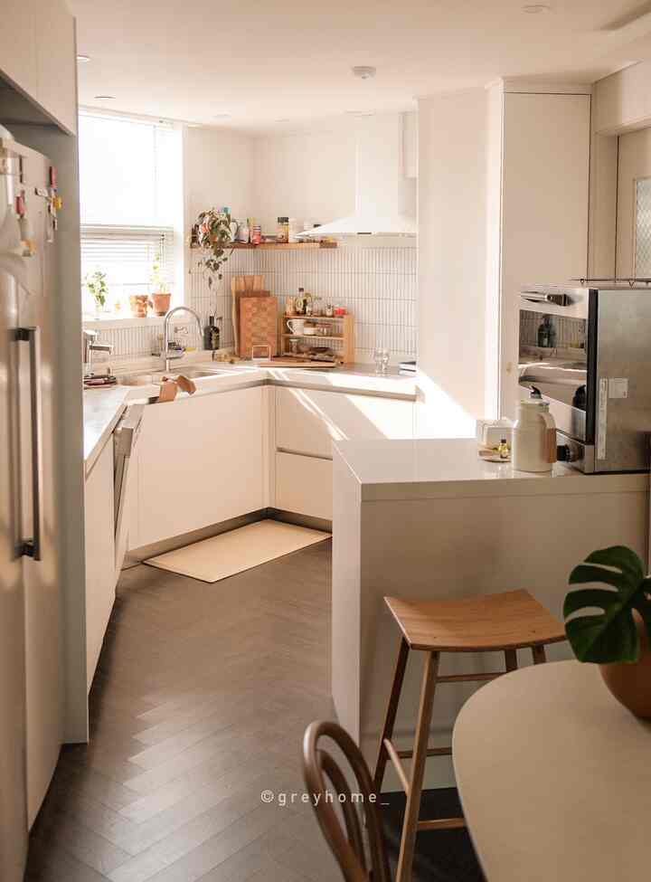 Bright white toned triangle kitchen featuring wood shelves and stools, creating a warm, organized kitchen space