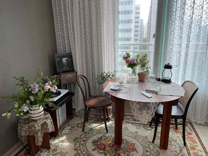 A small dining room in white and brown tones featuring a floral rug and lace curtains creating a classic and calm atmosphere