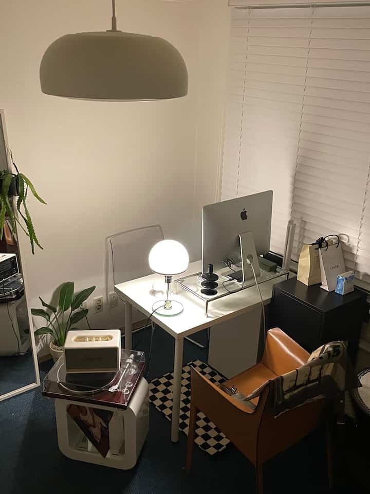 Natural and white toned home office featuring modern desk, leather chair, lighting, blinds, and plants creating a cozy workspace