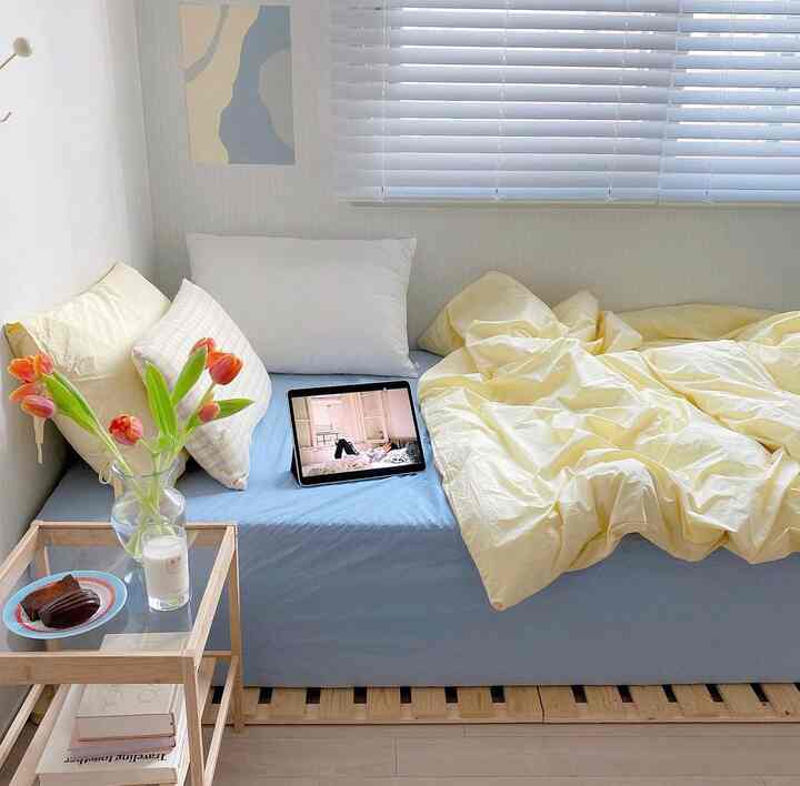 柔らかな黄色と青のトーンの寝室、木製のナイトテーブルとポスターが配置された居心地の良い雰囲気