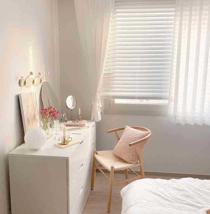 Bright white-toned bedroom featuring a dresser and a natural rattan chair creating a cozy atmosphere