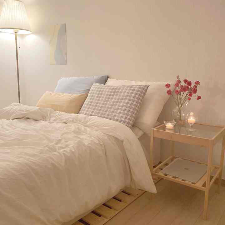 アイボリー色調の寝室、木製ベッドとナイトテーブルにキャンドルを置き、温かみのある雰囲気のインテリア