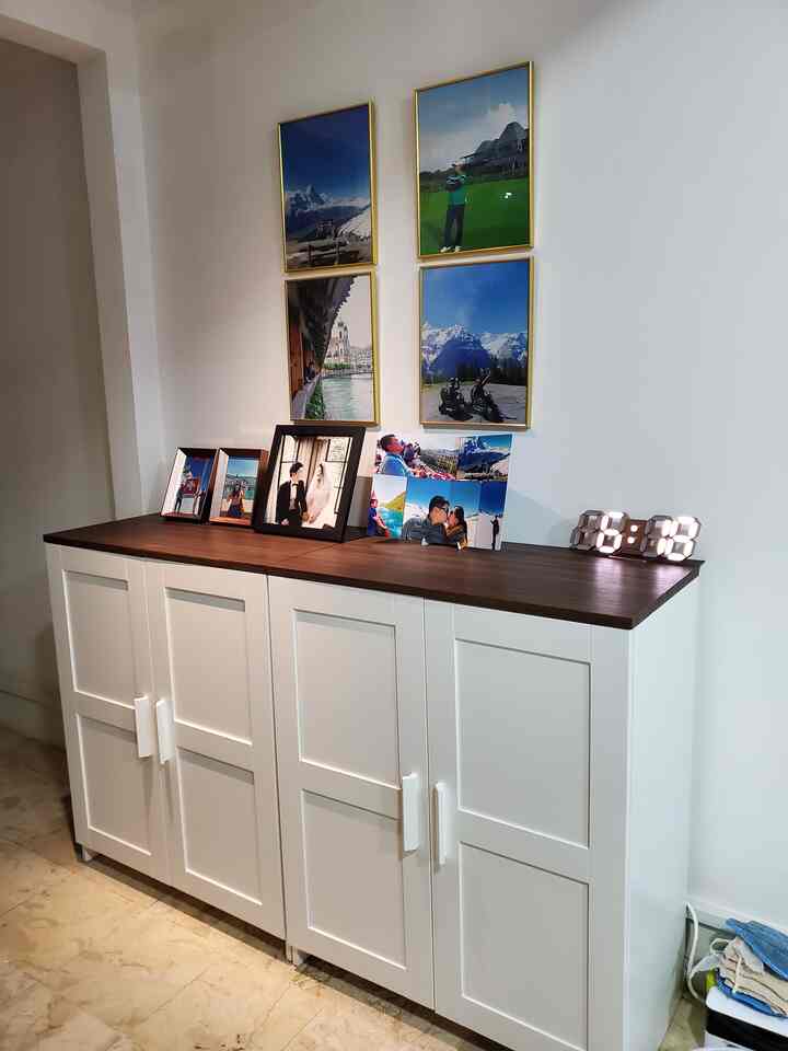 A living room with white walls and brown wooden top BRIMNES door cabinet featuring photo frames and an LED clock creating a warm photo zone