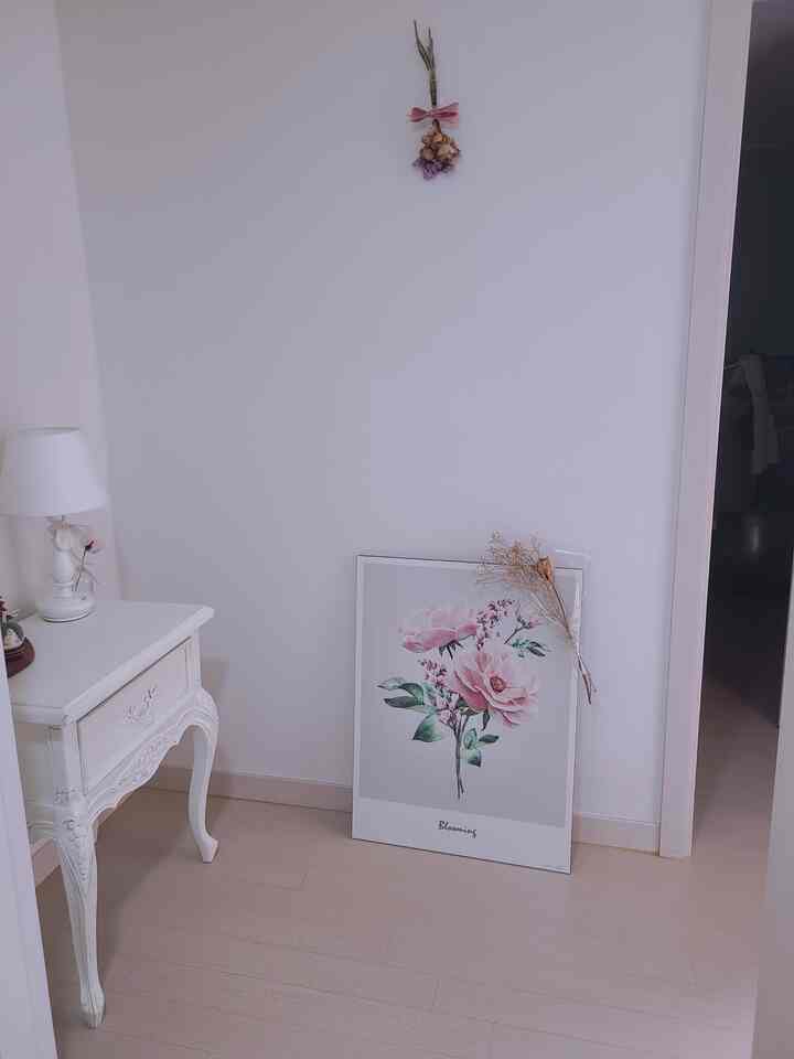 Entrance area with white and cream wood tones featuring floral artwork and vintage-style nightstand creating a cozy atmosphere