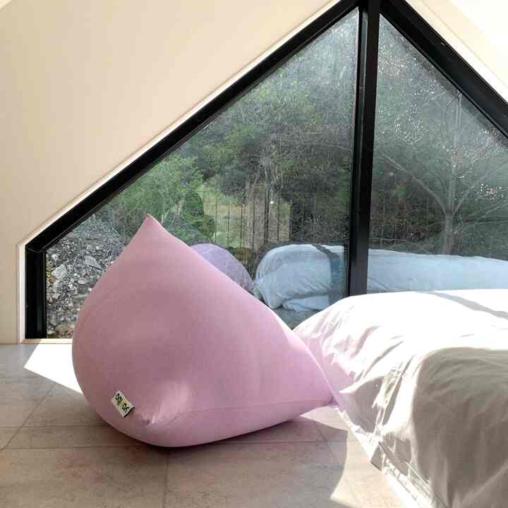Bedroom space with pink bean bag and white bedding illuminated by natural light