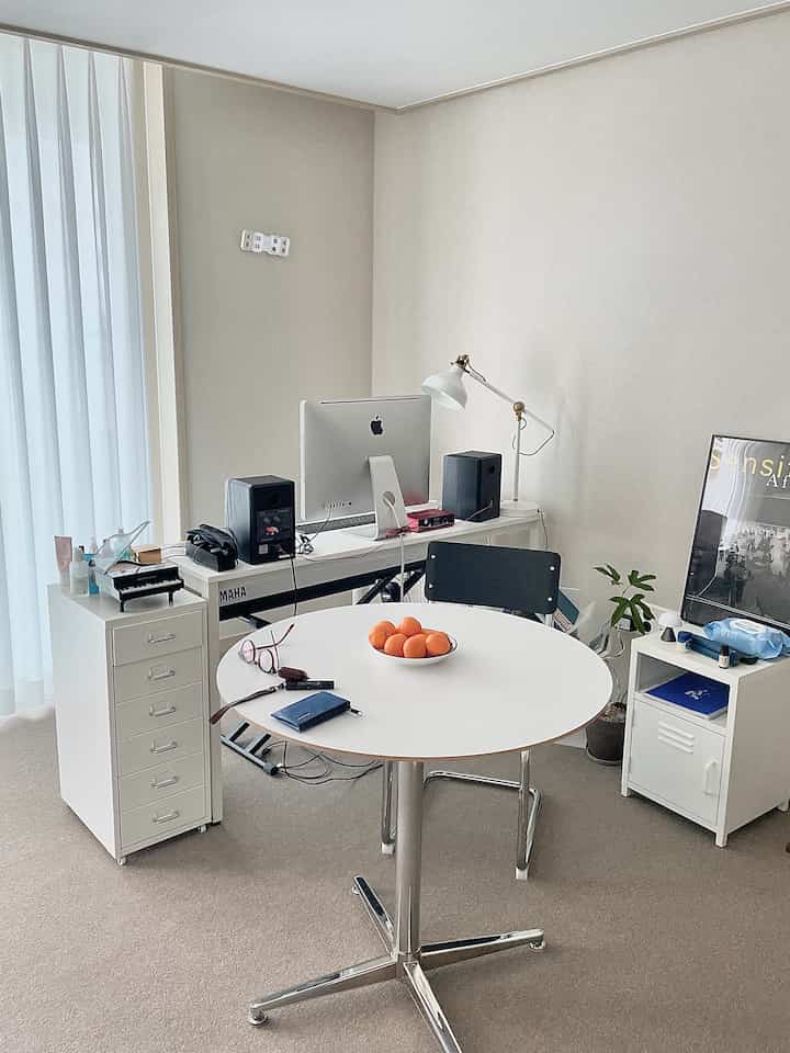 Natural-tone studio apartment living room featuring white dining table, desk with computer, and poster creating a tidy home office space