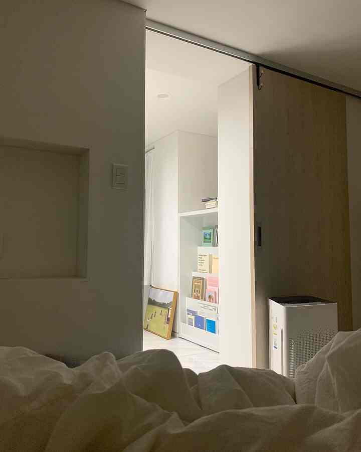 White-toned bedroom featuring a full bookshelf and air purifier, creating a neat and cozy atmosphere