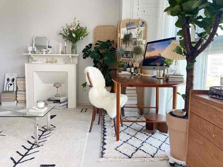 ホワイトとブラウンのトーンのワンルームホームオフィス兼リビング、ヴィンテージ家具とラグ、植物が配置されたナチュラルな印象的な空間