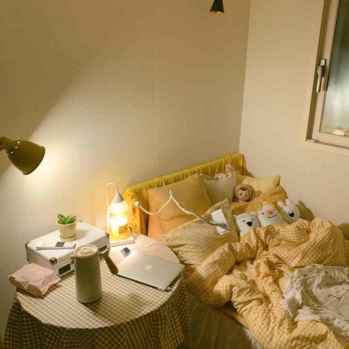 Warm yellow-toned bedroom featuring bed, cushions, and a table lamp creating a cozy atmosphere
