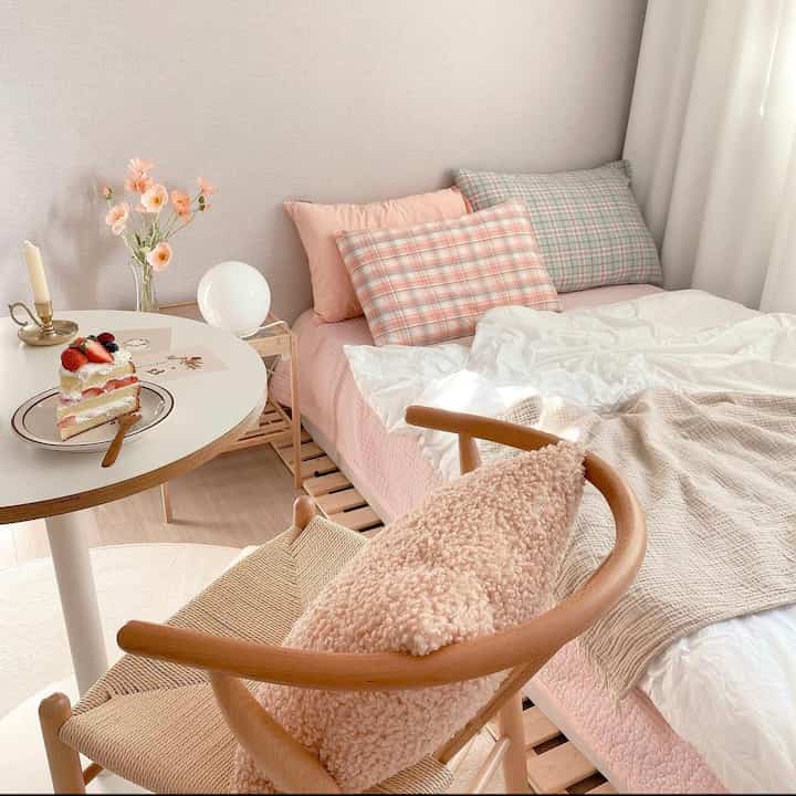 ピンクとナチュラルな色調の寝室、枕とクッションが配置された印象的な暖かいインテリア