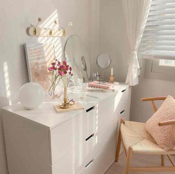White and natural toned powder room featuring a vanity, mirrors, dresser, and beige cushion creating a cozy atmosphere