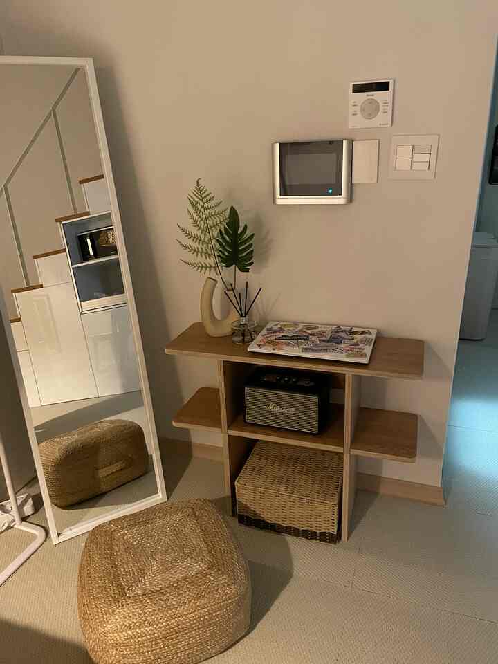 柔らかなベージュ調の玄関スペース、木製棚と収納、自然素材のプフが配置された自然な雰囲気のインテリア