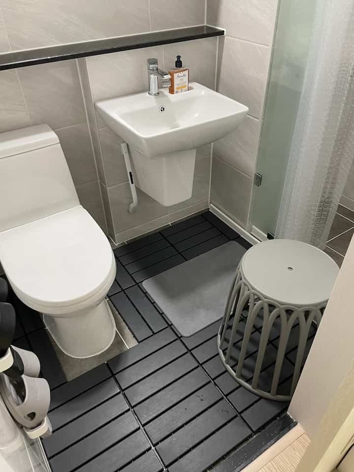 White and black toned bathroom featuring sink, toilet, stool, and bath mat in a clean space