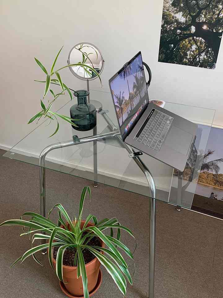 Minimal home office with transparent glass desk and metal legs, featuring green plants and decorative items enhancing calm ambiance