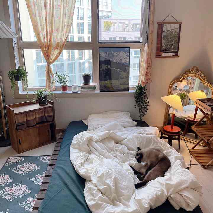 Bright yellow curtains and white bedding in a single bedroom featuring natural wooden furniture and plants, creating a cozy atmosphere