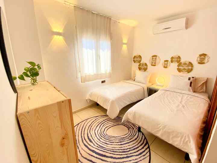 白とベージュのトーンの二人用ゲストルーム、木製家具と丸いラグが配置されたミニマルでナチュラルな雰囲気のあるインテリア