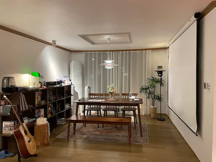 白とブラウンのナチュラルトーンのダイニング兼書斎、ペンダントライトと大型プロジェクタースクリーンが配置された雰囲気のある空間