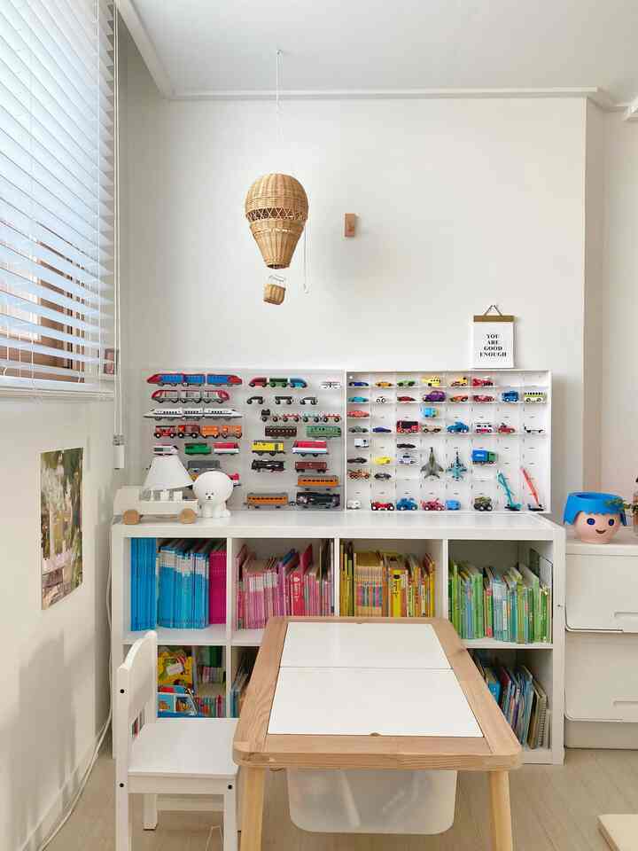 Bright kids' room with white and natural tones featuring bookshelves and organized toy storage, creating a clean cozy atmosphere