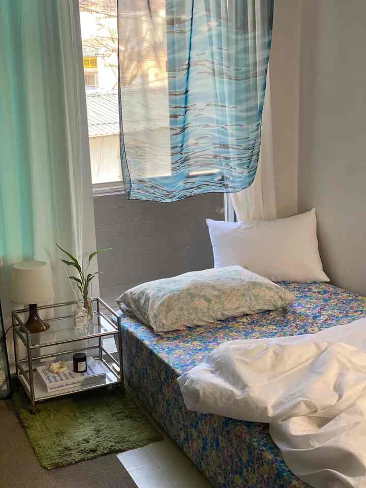 White and blue toned studio bedroom featuring floral bed and translucent blue curtain with natural atmosphere