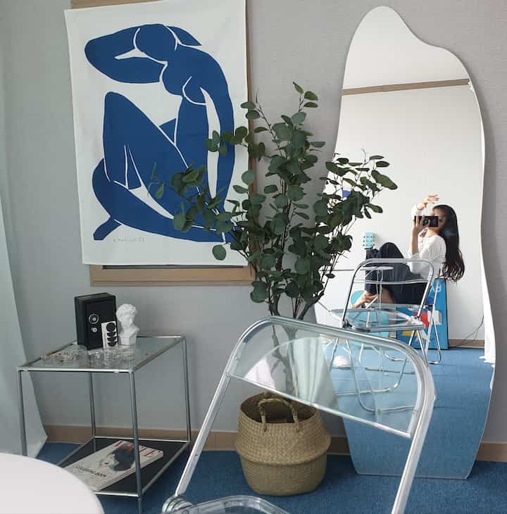 Blue-toned carpeted living room featuring a simple transparent folding chair, silver dollar eucalyptus plant, and vintage objet creating a modern aesthetic