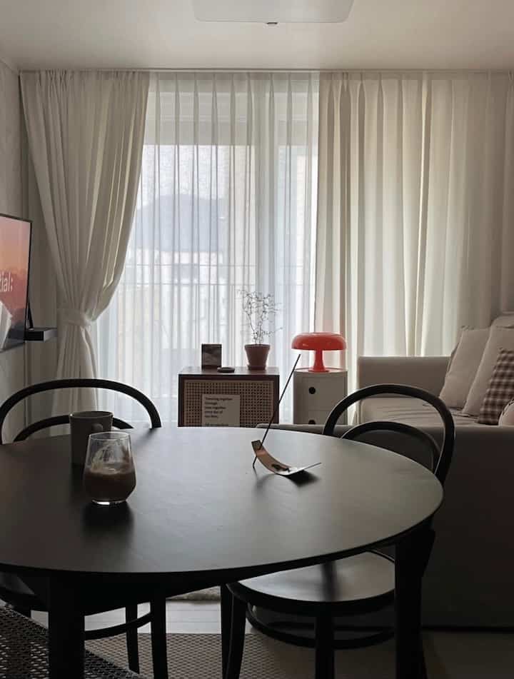 Soft white-toned living and dining room featuring a round dining table and beige sofa with simple, natural design
