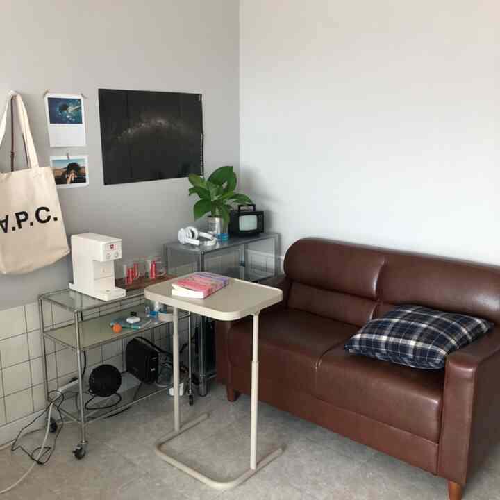 明るいベージュとブラウンのトーンのリビング、ブラウンレザーのソファと高さ調節可能なサイドテーブルが配置されたシンプルな空間