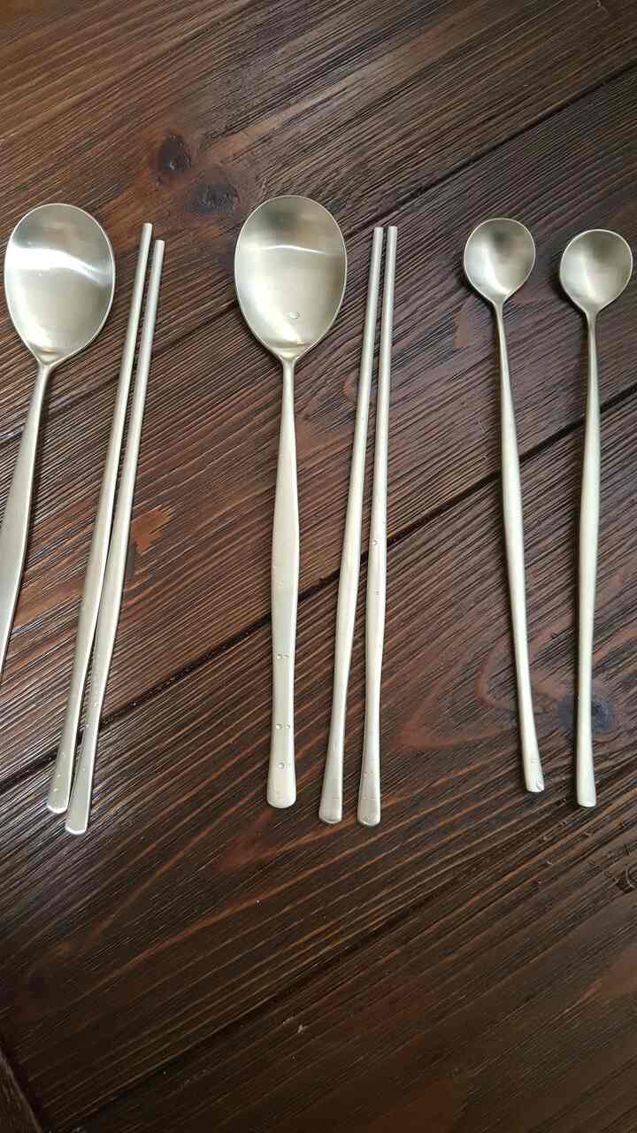 Gold-toned long spoons and chopsticks cutlery set placed on wooden dining table