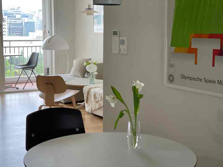 明るく自然なホワイトとベージュのトーンのリビングとキッチンスペース、円形テーブルと洗練されたモダンな家具が配置された印象的なインテリア