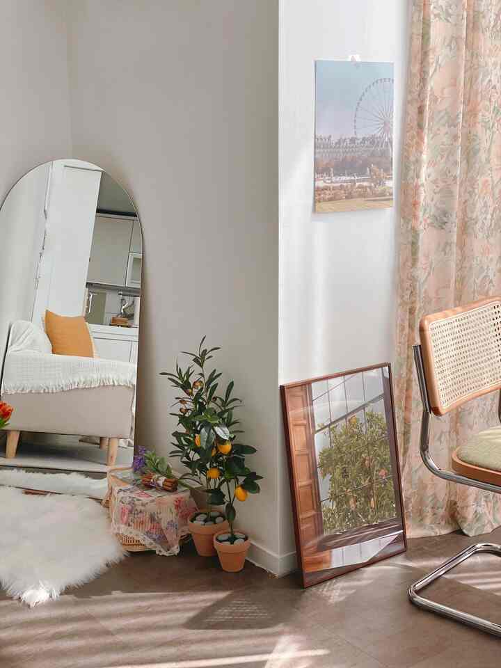 Natural-toned living room featuring beige sofa, large arched full-length mirror, potted plants, and floral curtains creating cozy ambiance