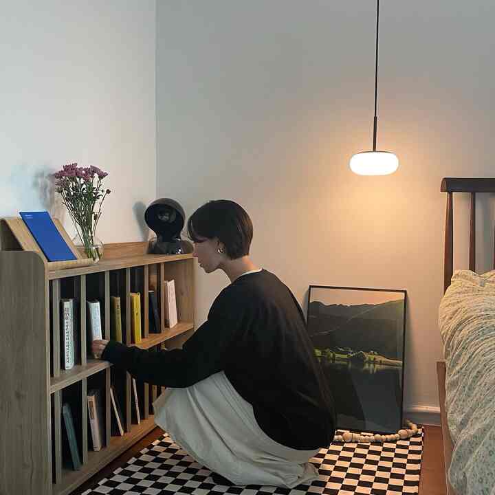 White-walled natural wood bedroom-study space featuring a checkered rug and warm ambient pendant lighting, cozy and minimalist vibe