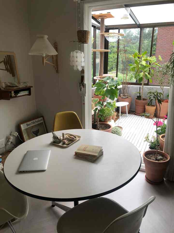 ナチュラルな白を基調としたリビングとベランダ、丸テーブルと多彩な植木鉢が配置された落ち着いた空間