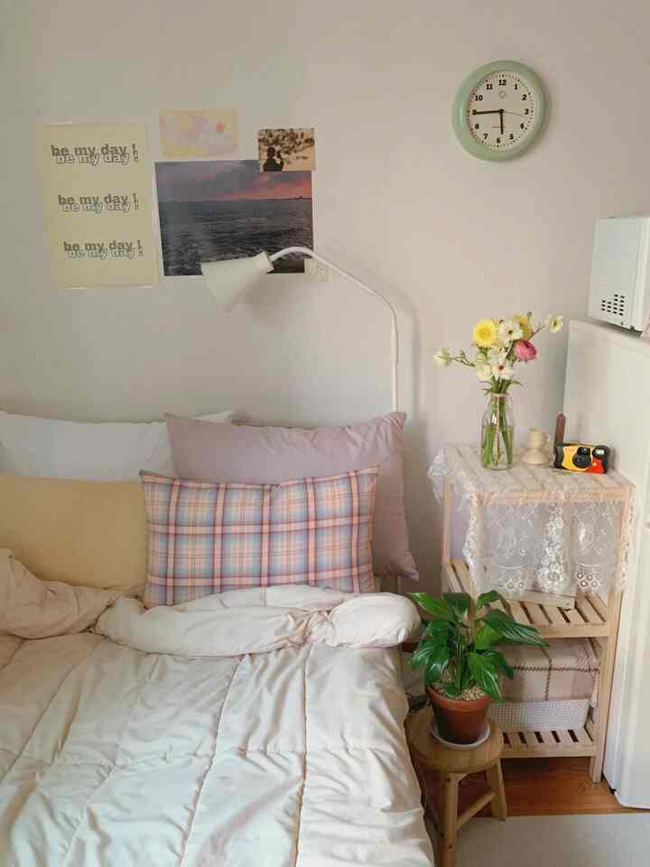 白とベージュを基調としたナチュラルな寝室、ファブリックの寝具と協テーブルの花瓶、壁時計、ポスターが配置された雰囲気のある空間