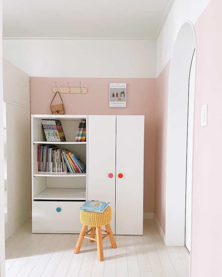 White and pink toned kids' room featuring bookshelf and storage cabinet, creating a cozy and neat atmosphere