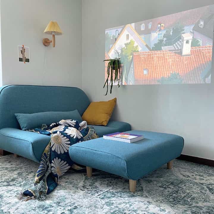 Bright white-walled compact studio featuring a blue fabric single sofa and ottoman with cozy atmosphere