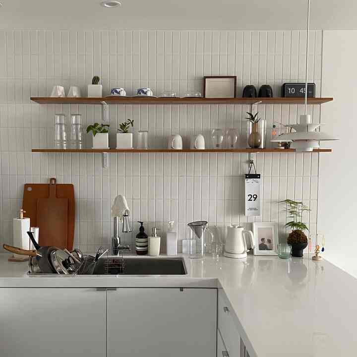 A simple kitchen with white surfaces and wood-toned shelves, featuring neatly arranged kitchen utensils and open shelving