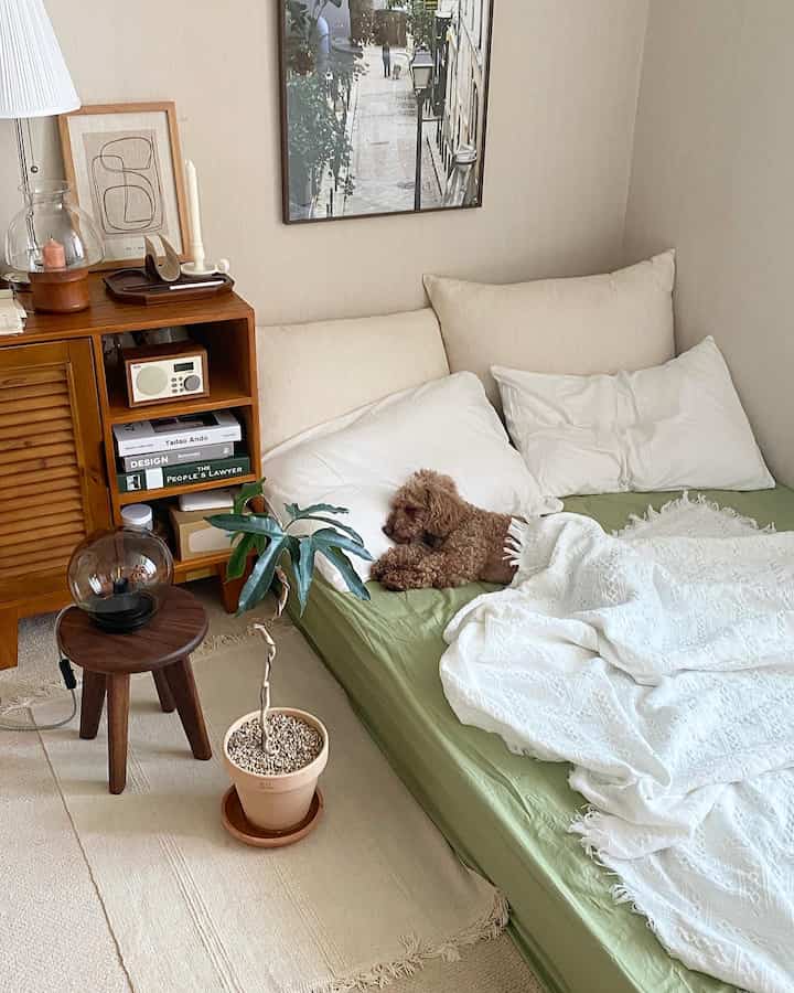 ナチュラルトーンの寝室、木製ナイトテーブルとグリーンのマットレスに犬がくつろぐ雰囲気のあるインテリア