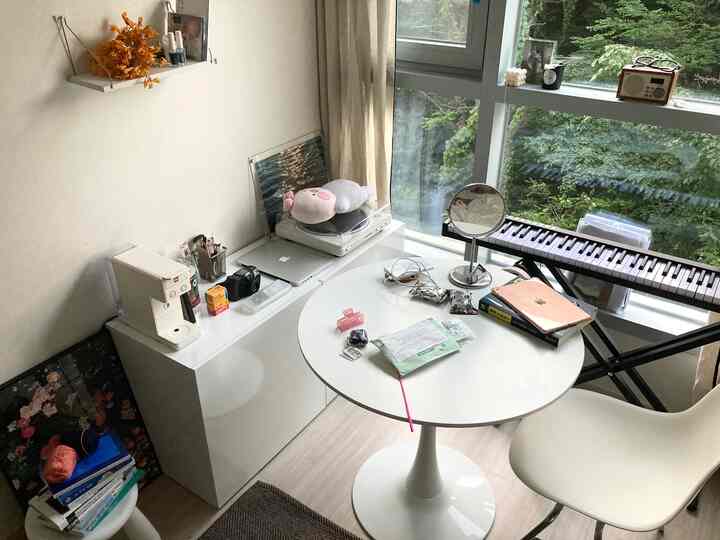 ホワイトとナチュラルカラーのリビング、丸いダイニングテーブルと椅子、電子ピアノ、コーヒーマシン、ポスターが配置された雰囲気のある空間