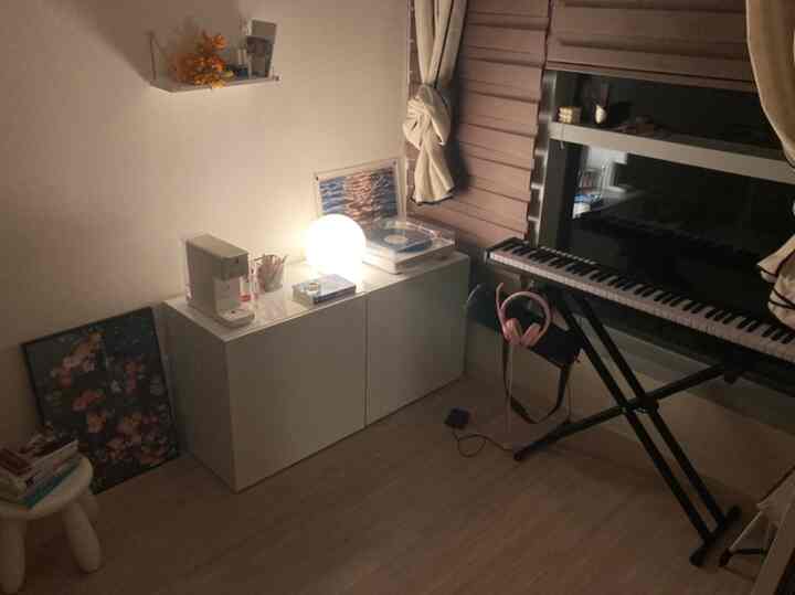 白を基調としたワンルーム、電子ピアノと照明が配置された雰囲気のある多目的ルーム