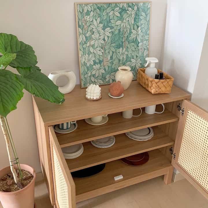 Natural wood tone corner storage cabinet against beige walls with dishes and decor items creating a warm atmosphere